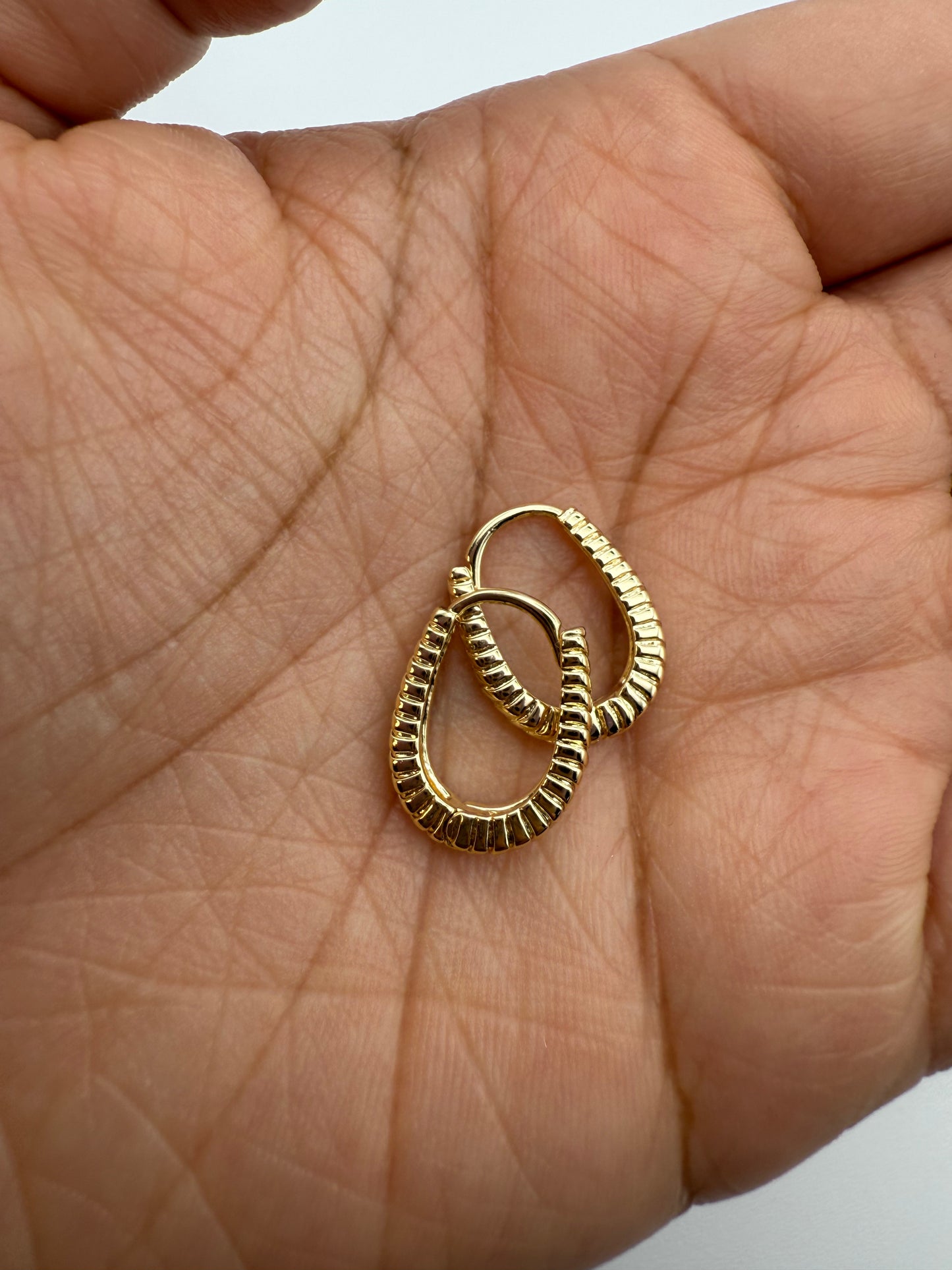 Gold huggie hoop earrings held in palm on a light skin background