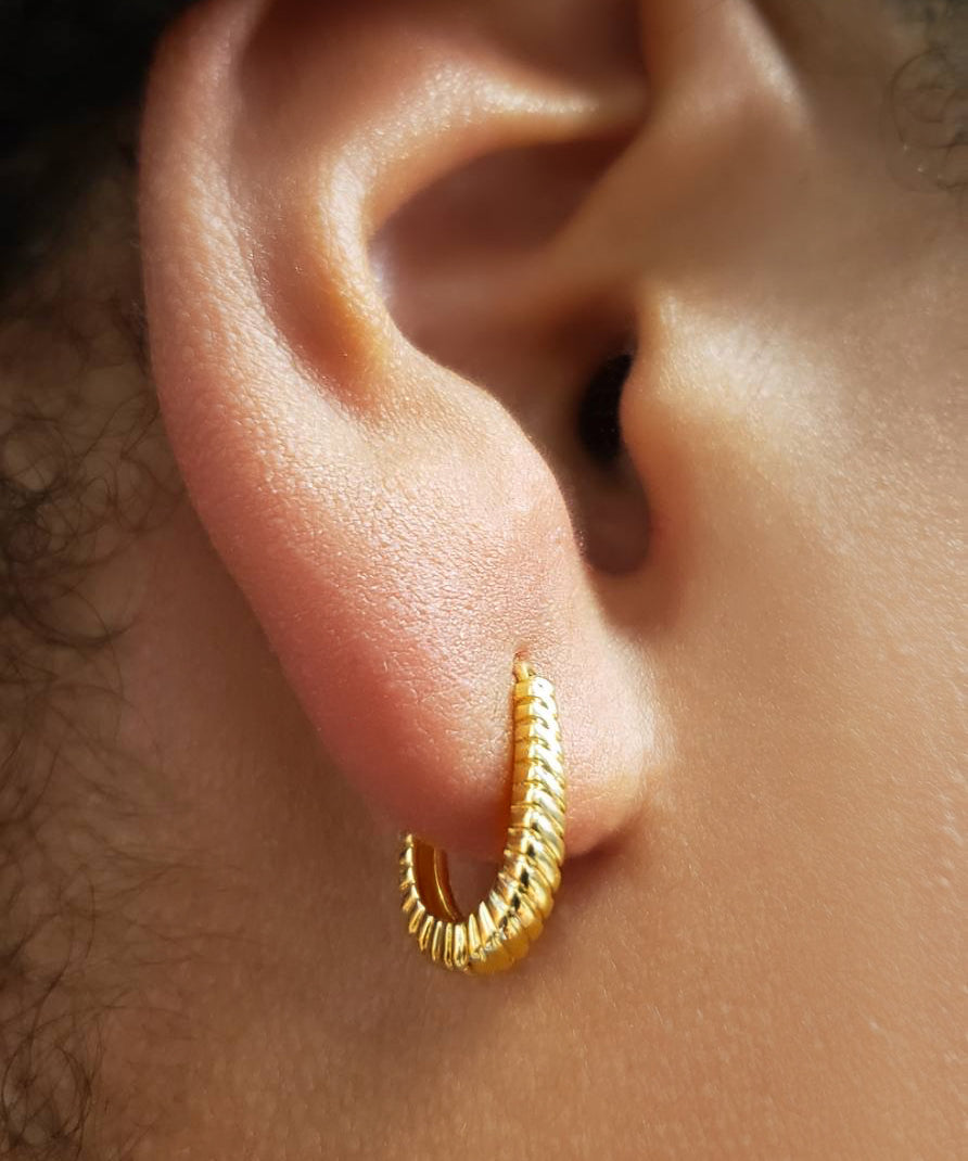 Close-up of an ear wearing a gold huggie hoop earring