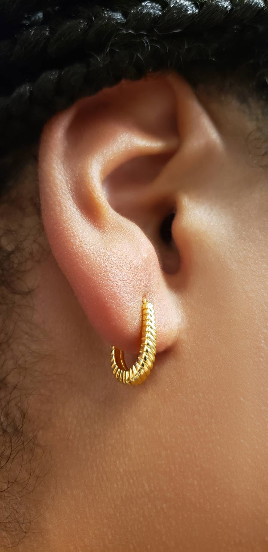 Close-up of an ear wearing a gold huggie hoop earring