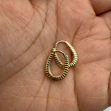 Gold huggie hoop earrings held in palm on a light skin background