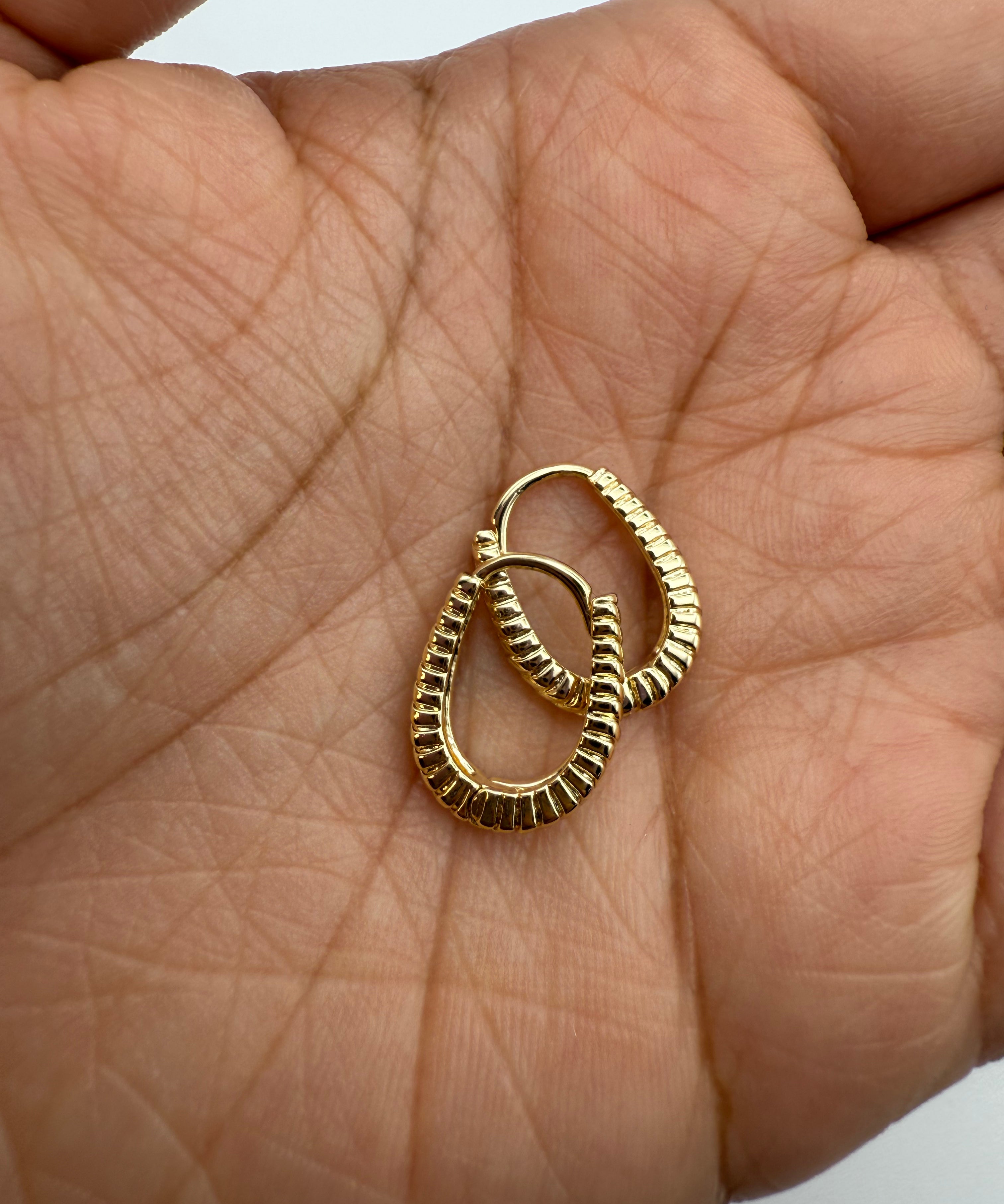 Gold huggie hoop earrings held in palm on a light skin background