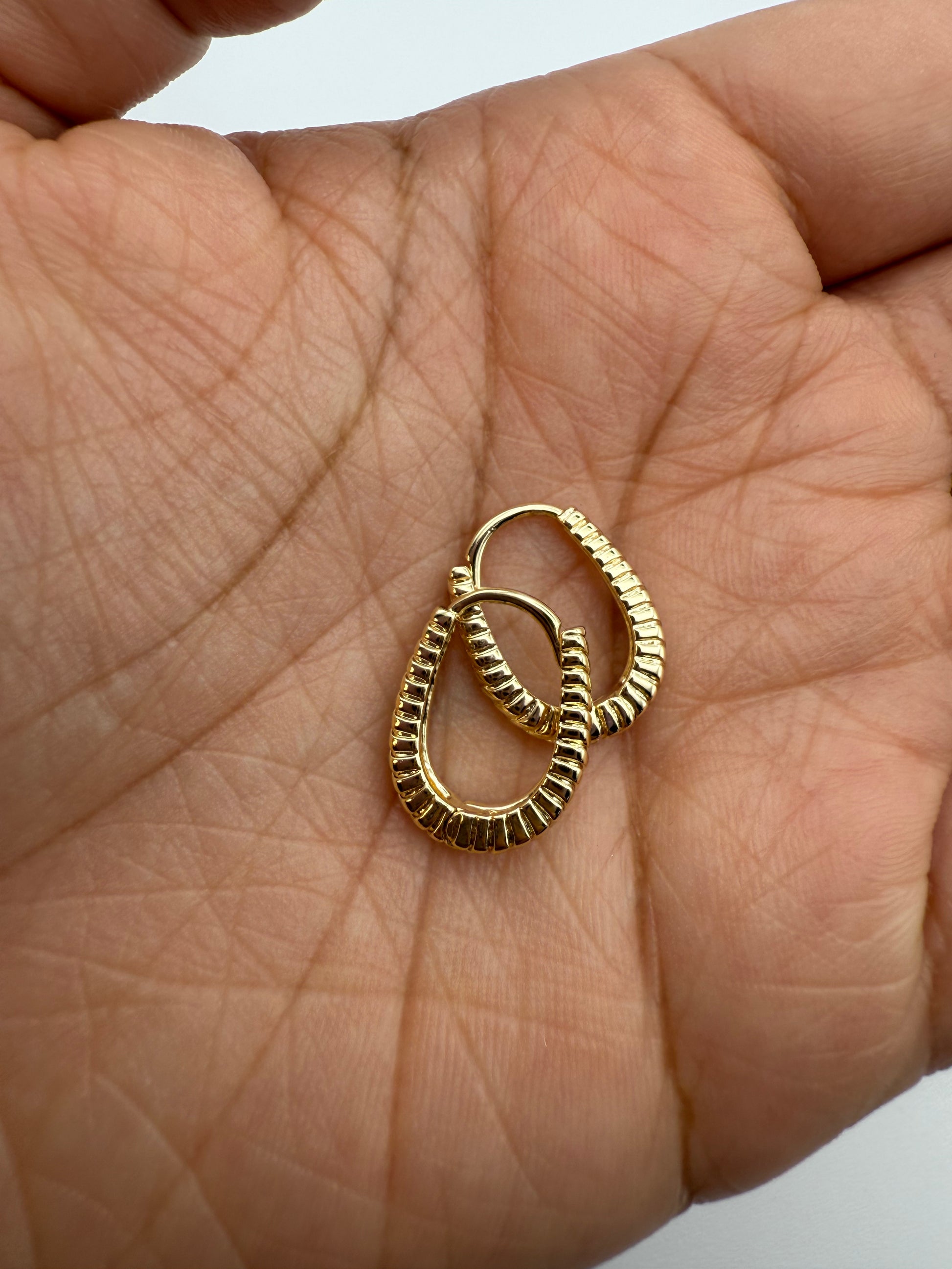 Gold huggie hoop earrings held in palm on a light skin background